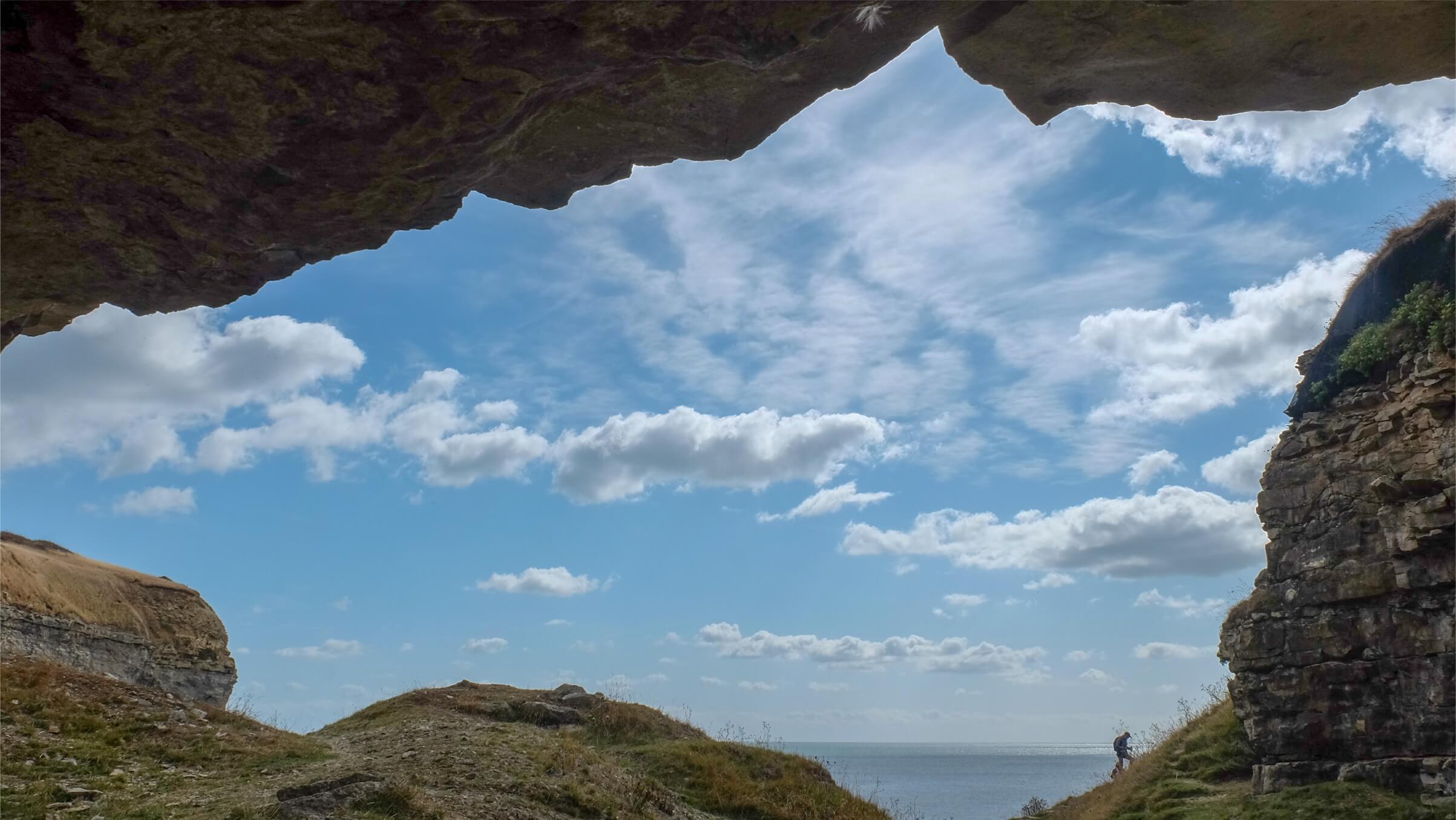 A walker climbs up a steep path on the rocky Jurassic coastline. The blue summer sky is dotted with small white cloudsT