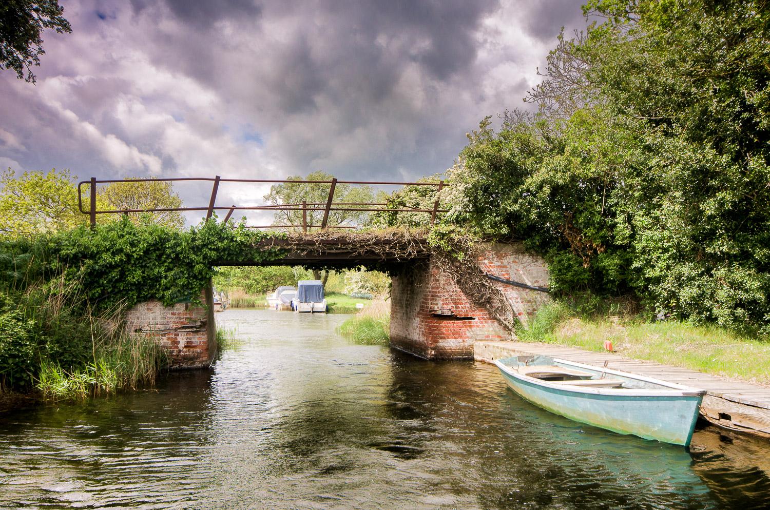 An old bridge, red bricks crumbling. railings rusted set against a stormy sky. A single boat is tied up to transport you.