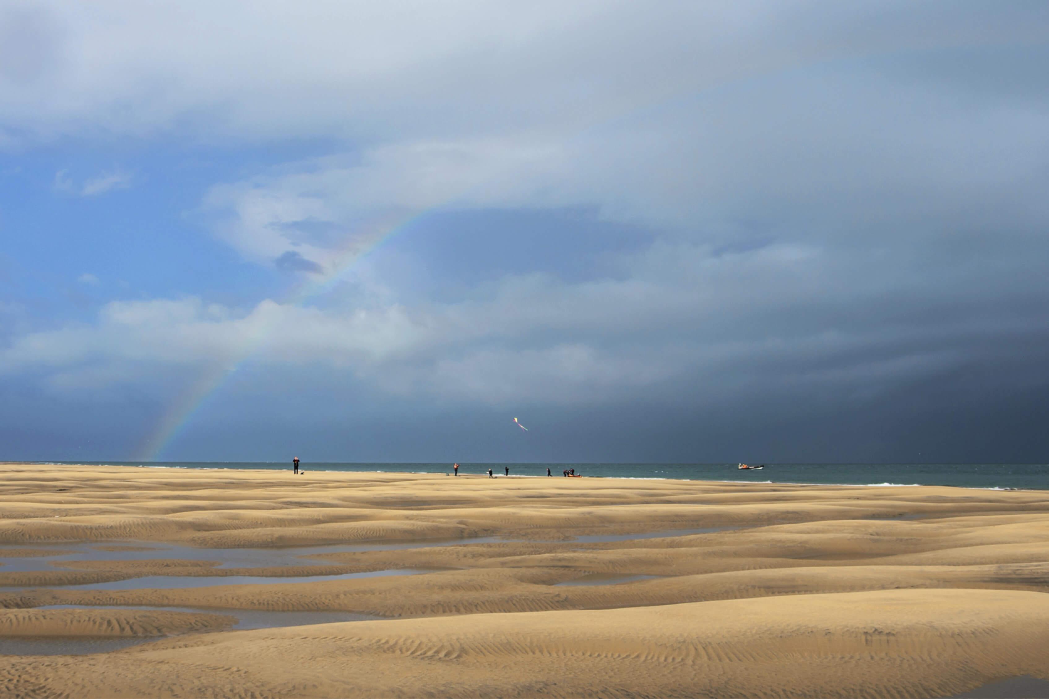 Rainbow arching across a grey stormy sky, undulating sandbanks moulded by the sea