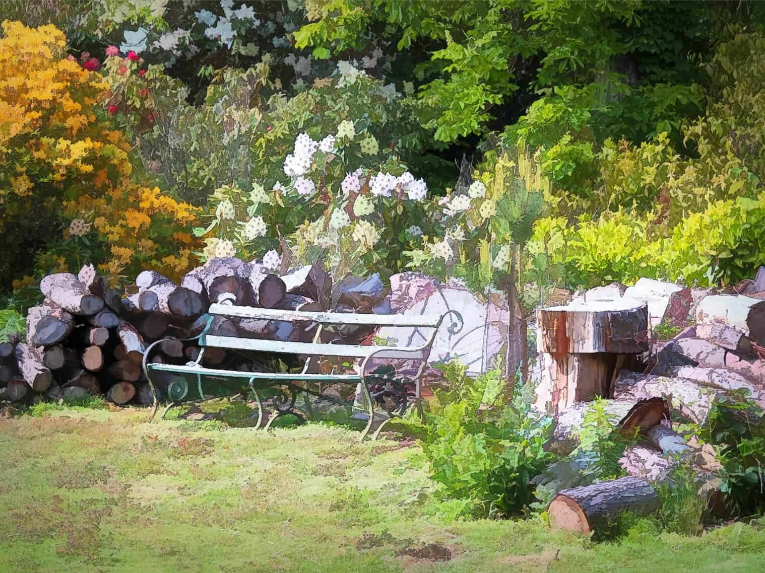 An old wrought iron garden seat on a green lawn surrounded by flowers in bloom and a piles of cut logs.