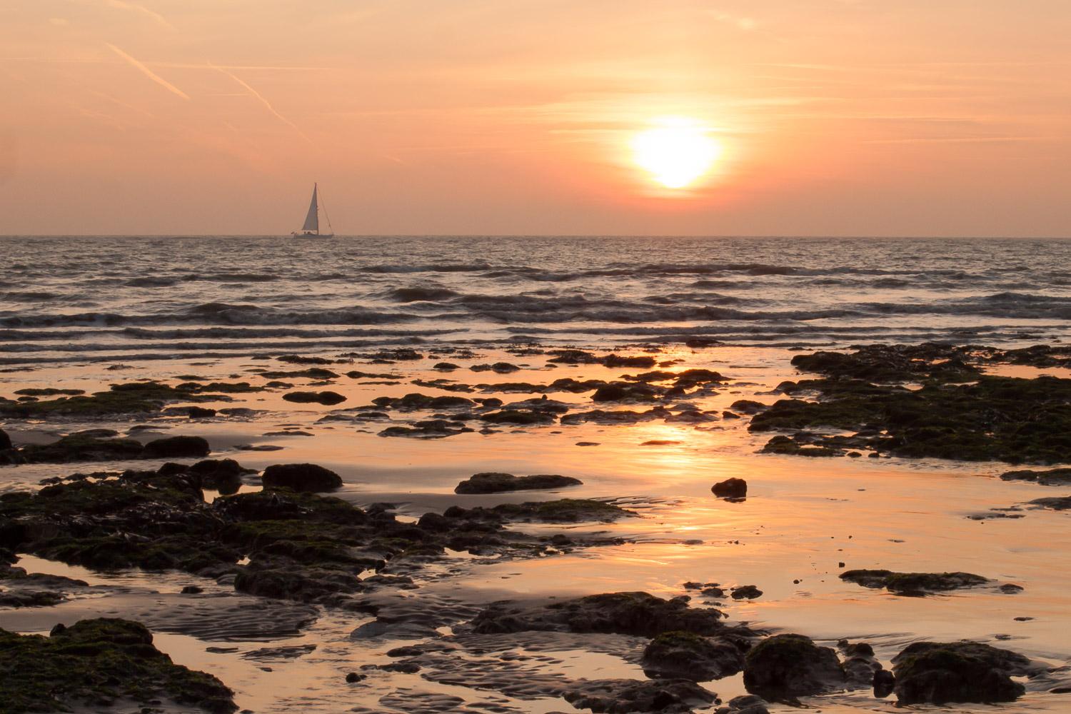 Sunrise over Kingsdown bay, rich colours reflect in wet sand, sailing boat on the horizon, sailing towards the sun.